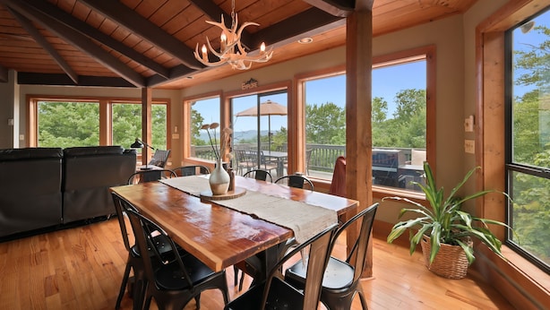 A spacious dining area with a wooden table, chairs, and a chandelier. Large windows offer views of the outdoors. - Beech Mt Place - Cool Mtn Escape & Big Views! (Beech Mountain)