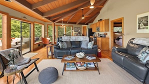 A spacious living area with a wooden ceiling, a sofa, a coffee table with books, and a view of the outdoors. - Beech Mt Place - Cool Mtn Escape & Big Views! (Beech Mountain)