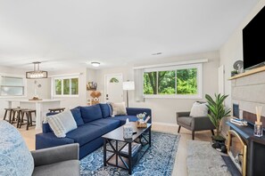 Un salon moderne avec un canapé bleu, une table basse et une cheminée. On y trouve également un coin repas avec une table blanche et des tabourets de bar.