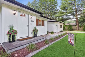 A row of white single-story houses with numbered doors, a well-maintained lawn, and a welcome sign.