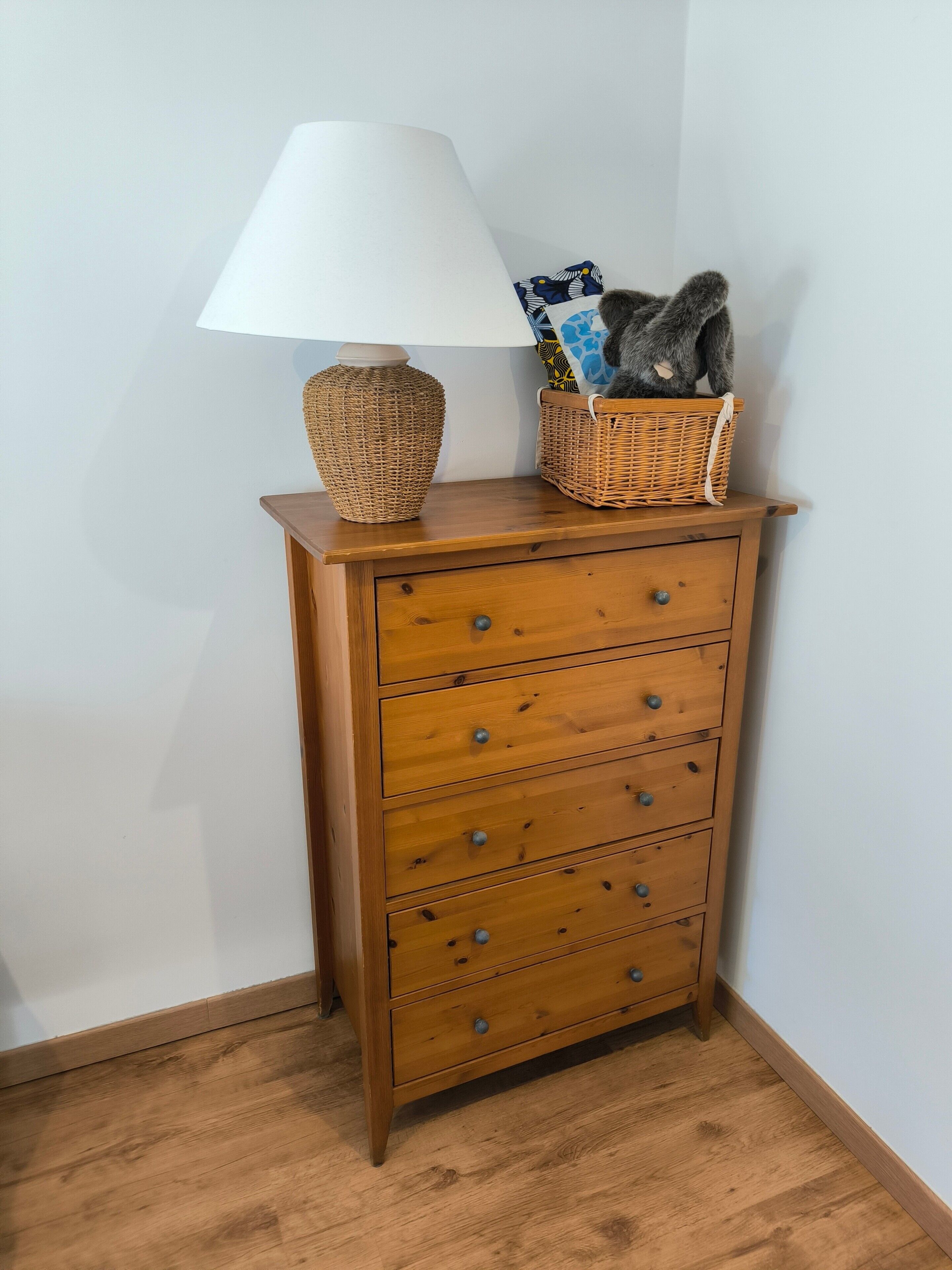 A wooden dresser with drawers, a lamp, and a basket with a stuffed animal.