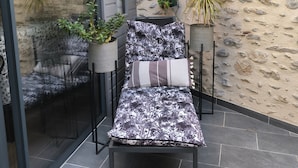 Een terras met een stoel, een bank en potplanten tegen een stenen muur.