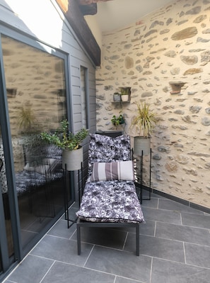 Un patio con una silla, un sofá y plantas en macetas frente a una pared de piedra.