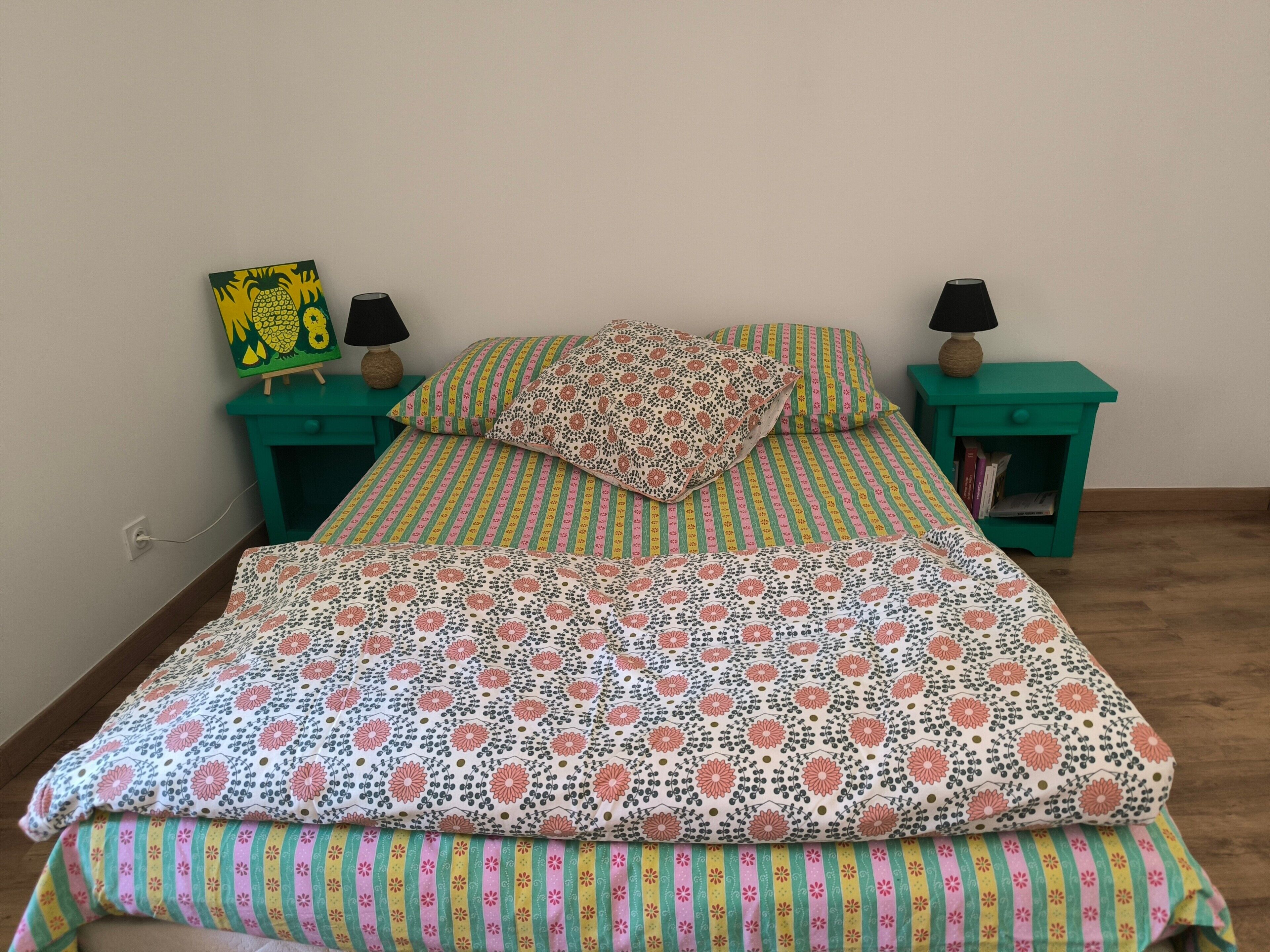 A bed with floral and striped bedding, two nightstands with lamps, and a wall-mounted picture.