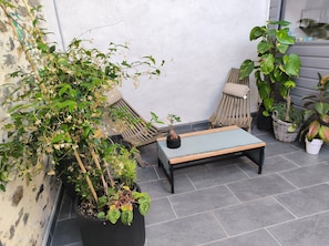 A patio with a black table, two wooden chairs, and various potted plants.