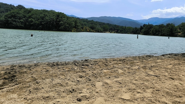 Een meer met een zandstrand, omgeven door dicht bos en bergen op de achtergrond.