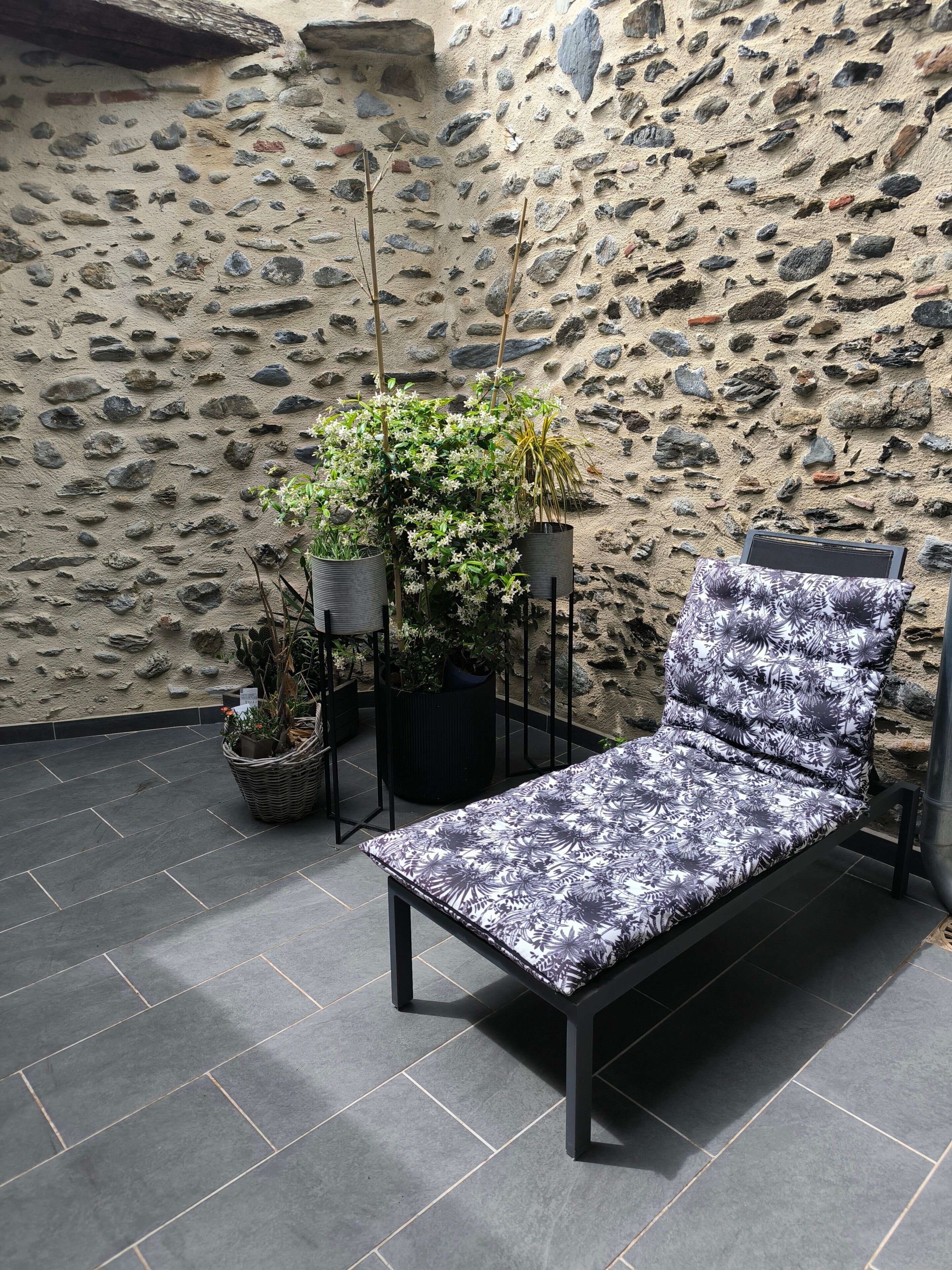 A stone wall, a black metal chair with a floral pattern, and potted plants.