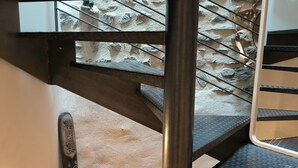 Een trap met een achtergrond van een stenen muur, metalen hekwerk en een houten bankje onderaan.