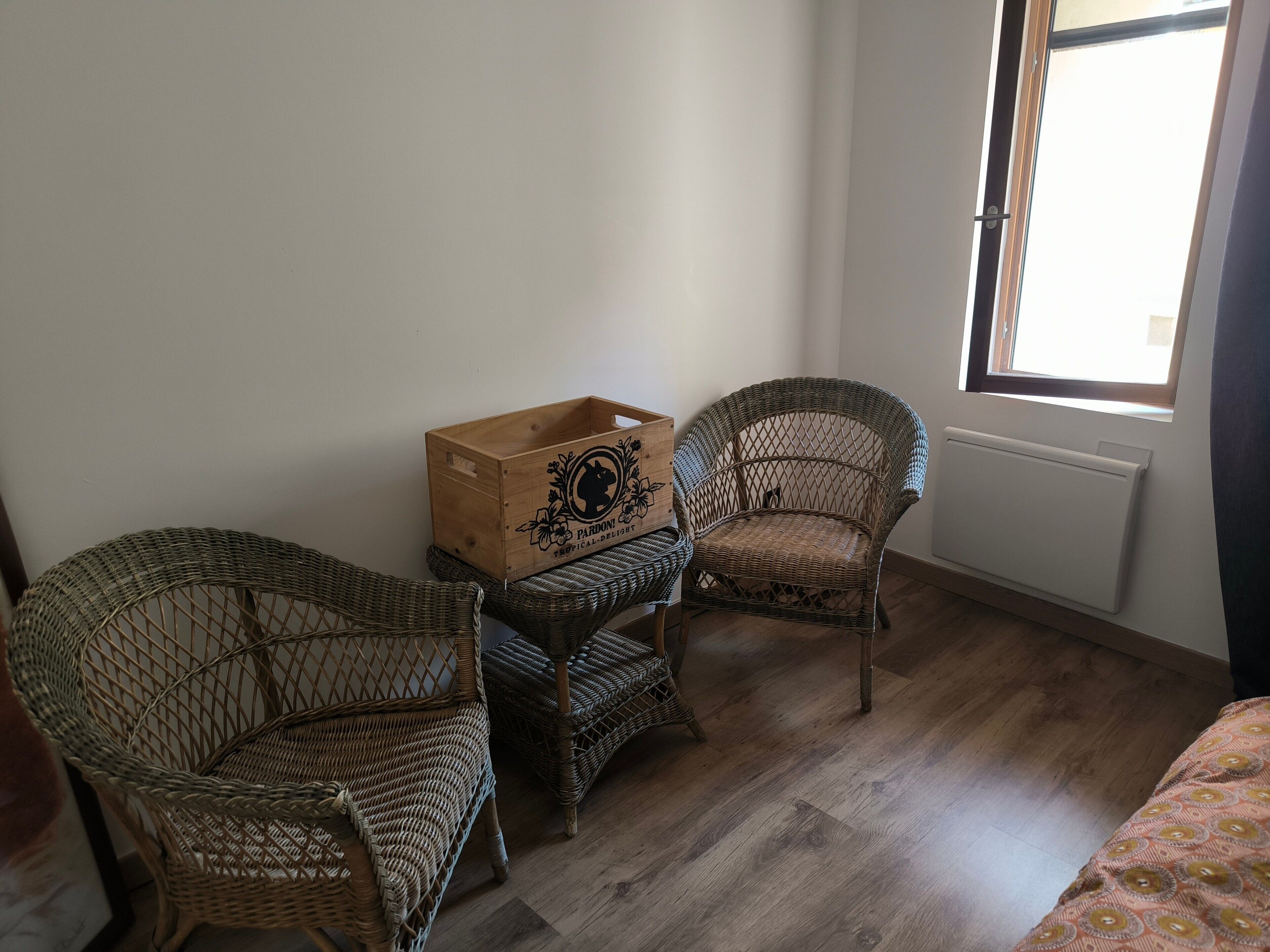 A room with two wicker chairs, a wooden crate, and a radiator.