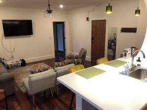 Ein modernes Wohnzimmer mit Flachbildfernseher, einer Couch, einem Esstisch und einer Küchenzeile mit Spüle.