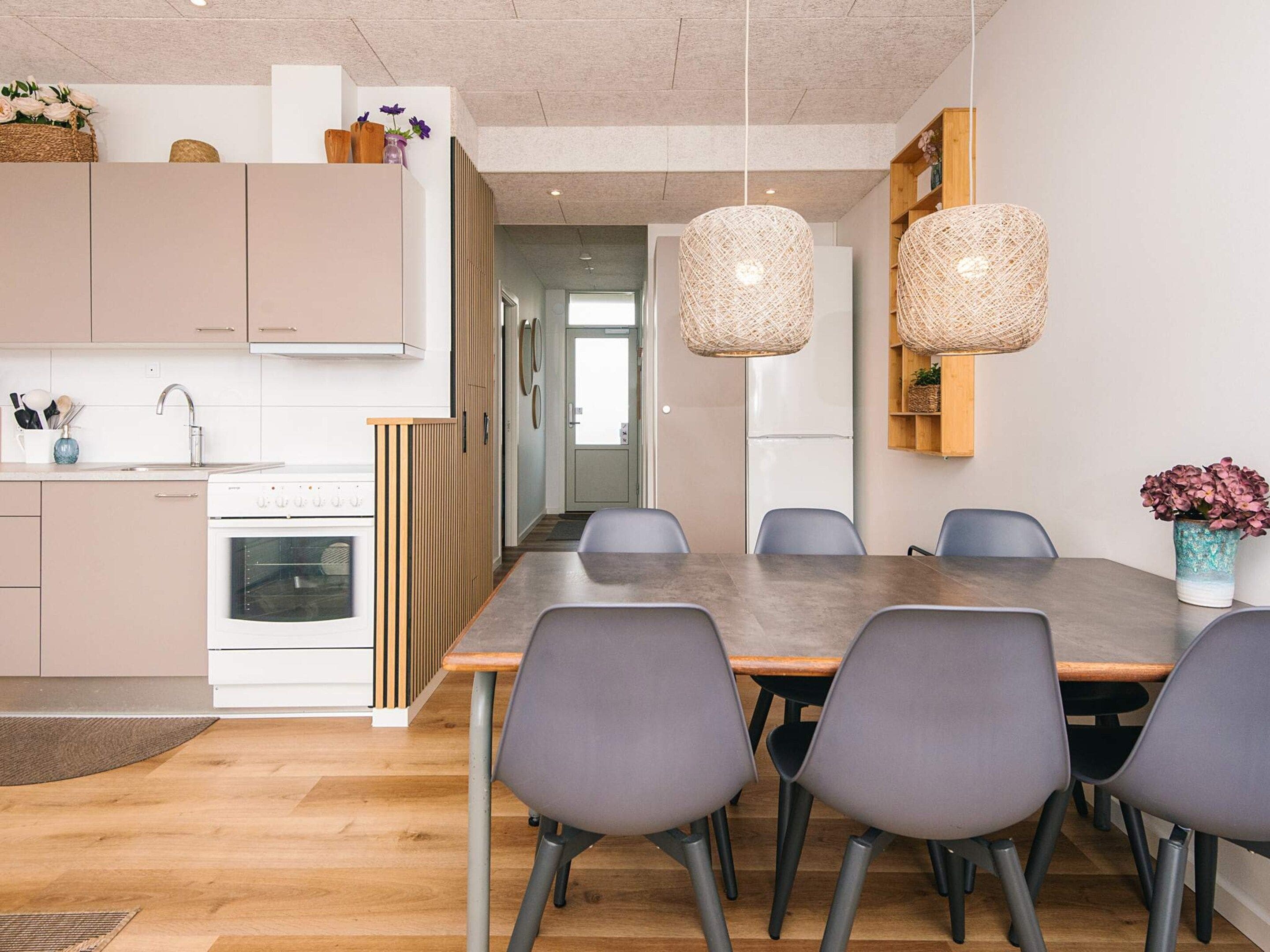 A modern kitchen with a dining area, featuring a large table and chairs, a refrigerator, and hanging light fixtures.