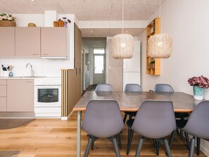 A modern kitchen with a dining area, featuring a large table and chairs, a refrigerator, and hanging light fixtures. - 4 Star Holiday Home in Fano (Fano)