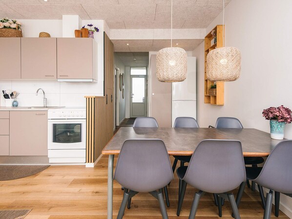 A modern kitchen with a dining area, featuring a large table and chairs, a refrigerator, and hanging light fixtures. - 4 Star Holiday Home in Fano (Fano)