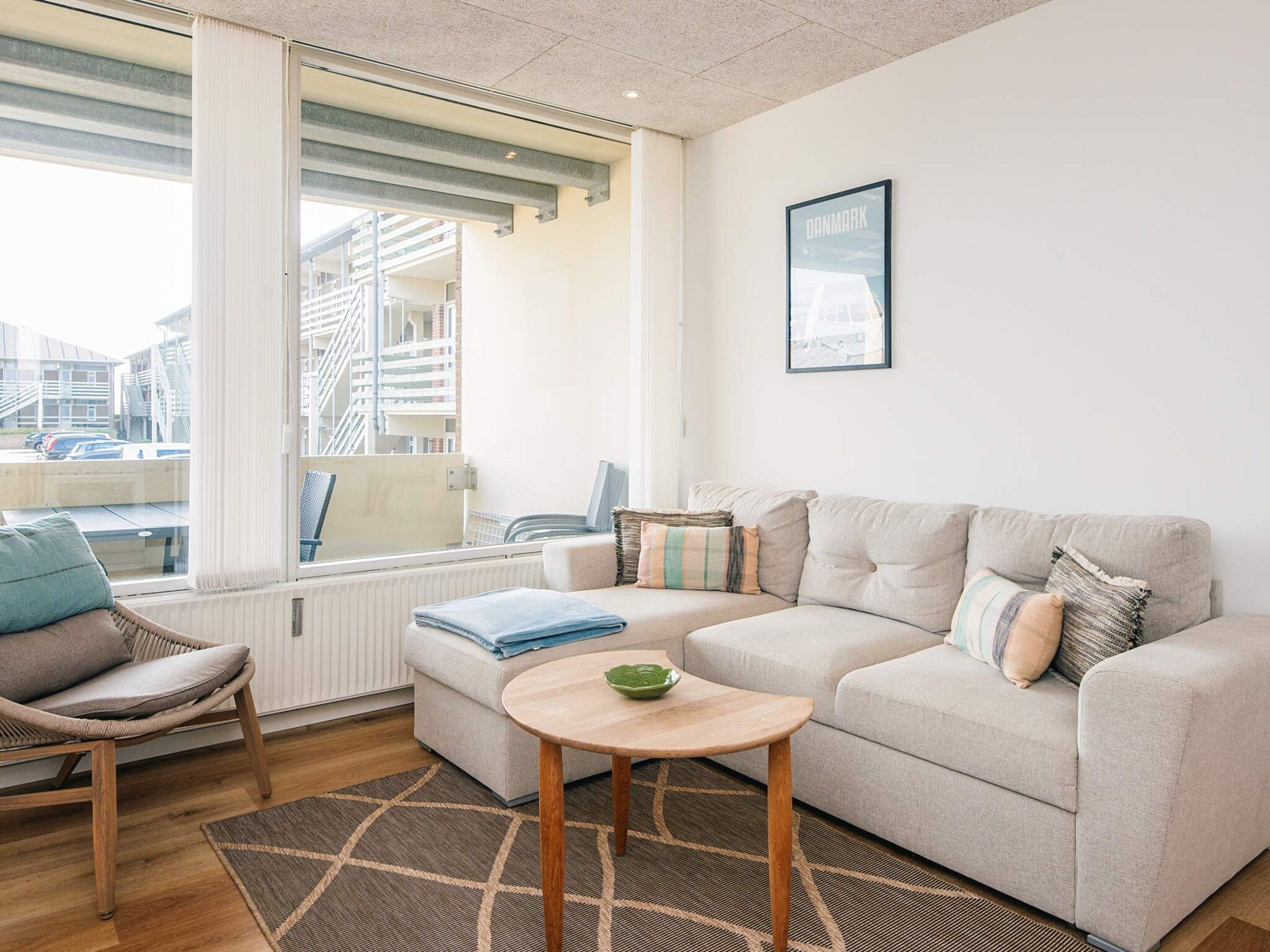 Ein modernes Wohnzimmer mit einer Couch, einem Sessel, einem kleinen Tisch und einem Fenster mit Jalousien.