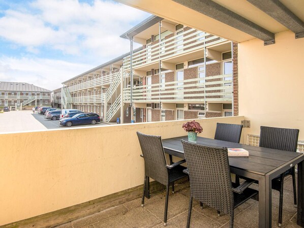 A balcony with a table and chairs, overlooking a parking area and a building with multiple floors and balconies. - 4 Star Holiday Home in Fano (Fano)