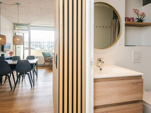 Ein modernes Interieur mit einer Holzwand, einem runden Spiegel, einem weißen Waschbecken und einem Essbereich mit Stühlen und einem Tisch.