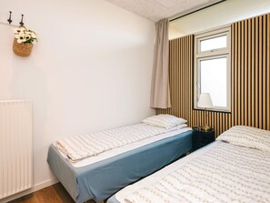 Ein Zimmer mit zwei Einzelbetten, einem Heizkörper, einem Fenster mit vertikalen Jalousien und einer Wandlampe.