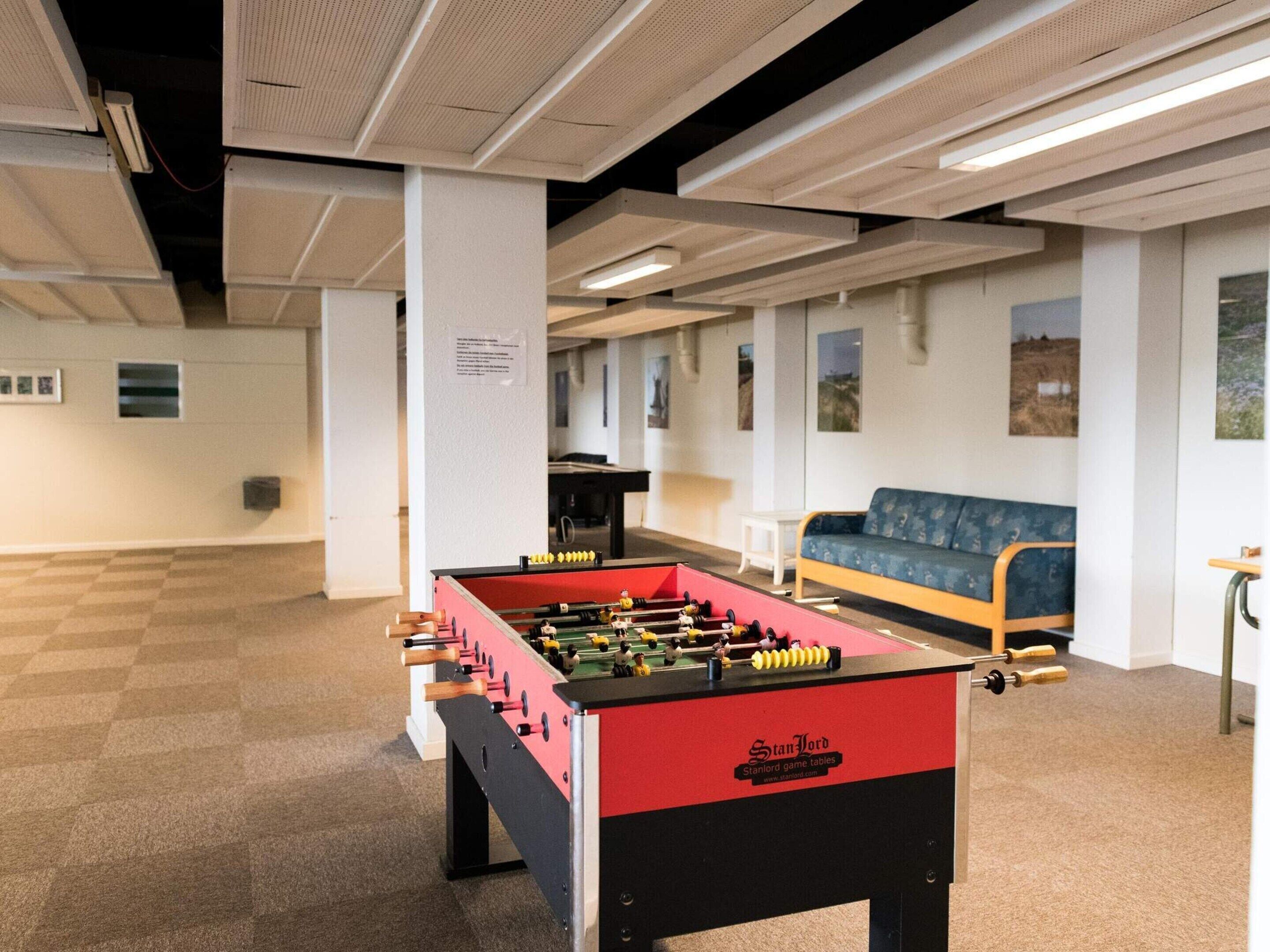 A room with a foosball table, a sofa, and a table tennis table.