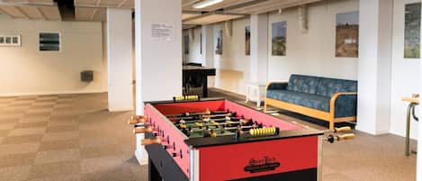 A room with a foosball table, a sofa, and a table tennis table.