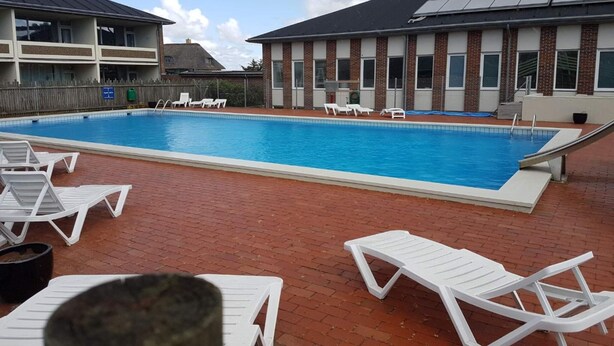 Une piscine avec des chaises longues et un bâtiment équipé de panneaux solaires.