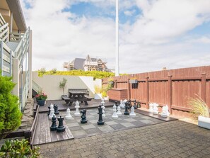 Ein Schachbrett steht auf einer gepflasterten Terrasse, neben einem hölzernen Bank und Blumentöpfen.