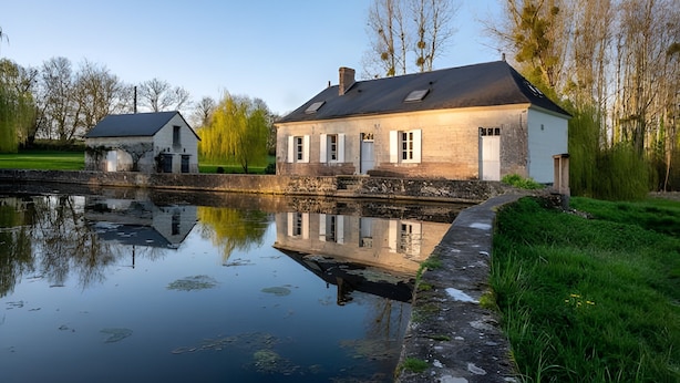 Et hus med stenvæg, en dam foran og træer i baggrunden.
