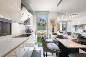 Eine moderne Küche mit Essbereich, einem über dem Tresen montierten Fernseher und Blick auf ein Gebäude durch die Tür.