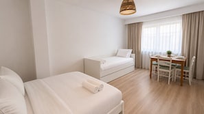 Ein modernes Hotelzimmer mit einem Bett, einer Couch, einem Esstisch mit Stühlen und einem Fenster mit Vorhängen.