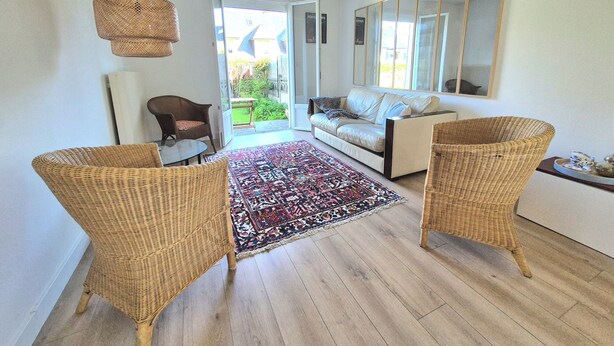 Ein stilvolles Wohnzimmer mit einer Couch, zwei Korbstühlen, einem gemusterten Teppich und einem großen Spiegel.