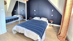 Ein Schlafzimmer mit einem Spiegelkleiderschrank, einem Bett mit gestreifter Bettdecke, einer Hängeleuchte und einer dunklen Akzentwand.