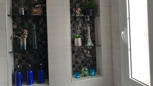 Un baño con salpicadero de azulejos, una ventana y estantes con artículos de tocador.