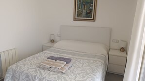 Una cama bien tendida con una colcha estampada, dos mesitas de noche con lámparas y un cuadro enmarcado sobre la cama.