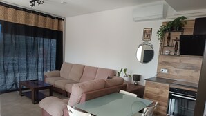 Una sala de estar moderna con un sofá, una mesa de comedor de vidrio y sillas. Hay una zona de cocina con estufa y microondas.