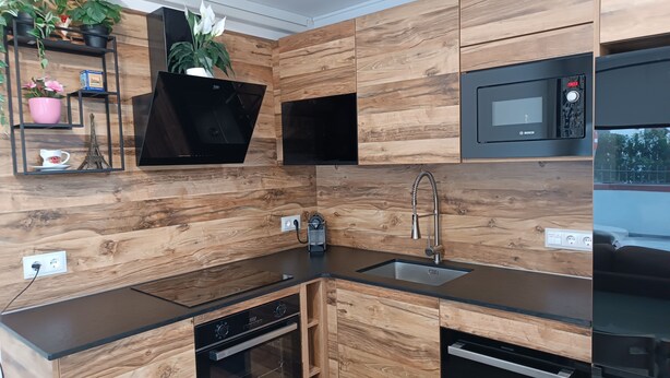 Una cocina moderna con armarios de madera, horno empotrado, lavavajillas, microondas y pileta.