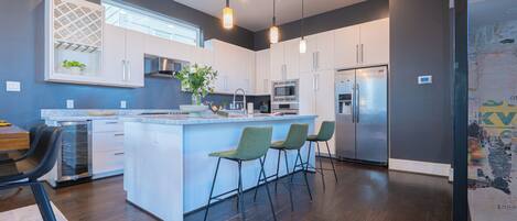 A modern kitchen with a central island, bar stools, and stainless steel appliances.