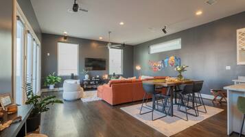 A modern living room with a sofa, dining table, and chairs, a ceiling fan, and a large window.
