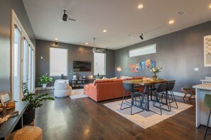 A modern living room with a sofa, dining table, and chairs, a ceiling fan, and a large window. - Stylish Townhome with Houston Skyline Views (Houston)