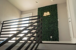 A staircase with a metal railing, a wall with a green wall-mounted plant, and a neon sign. - Stylish Townhome with Houston Skyline Views (Houston)