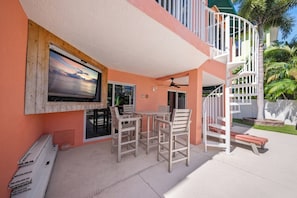 A covered outdoor area with a TV mounted on a wooden frame, a table with chairs, and a white spiral staircase.