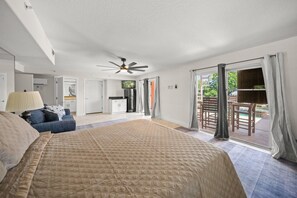 A bedroom with a large bed, a ceiling fan, a view of the outdoors, and a sliding glass door leading to a balcony.