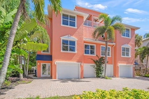 A multi-story residential building with a garage, surrounded by tropical vegetation.