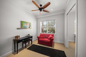 A room with a ceiling fan, a red sofa, a small table with a plant, a window with blinds, and a black rug.