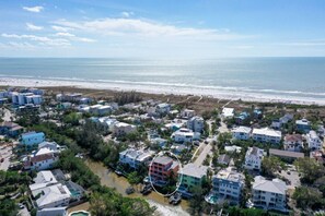 An aerial view of a coastal residential area with houses, a beach, and a river.