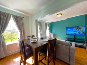 A dining area with a table set for four, a sofa, and a television on a stand. - Stylish Hotel Style Suite in Geneva`s Uptown Row (Geneva)