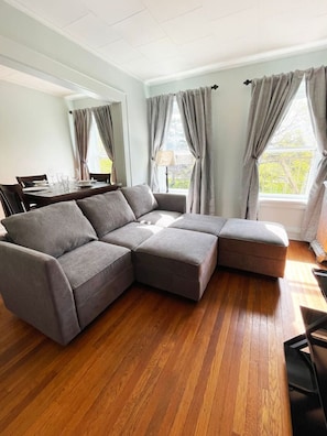 A modern living room with a sectional sofa, a dining table, and a view of the outdoors.