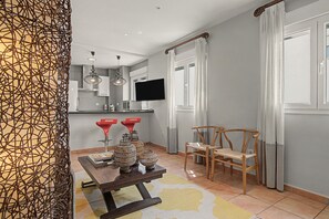 A modern living room with a dining area, a TV mounted on the wall, and a window with curtains. - Mirador del Palmar Suite – Free Parking (Conil de la Frontera)