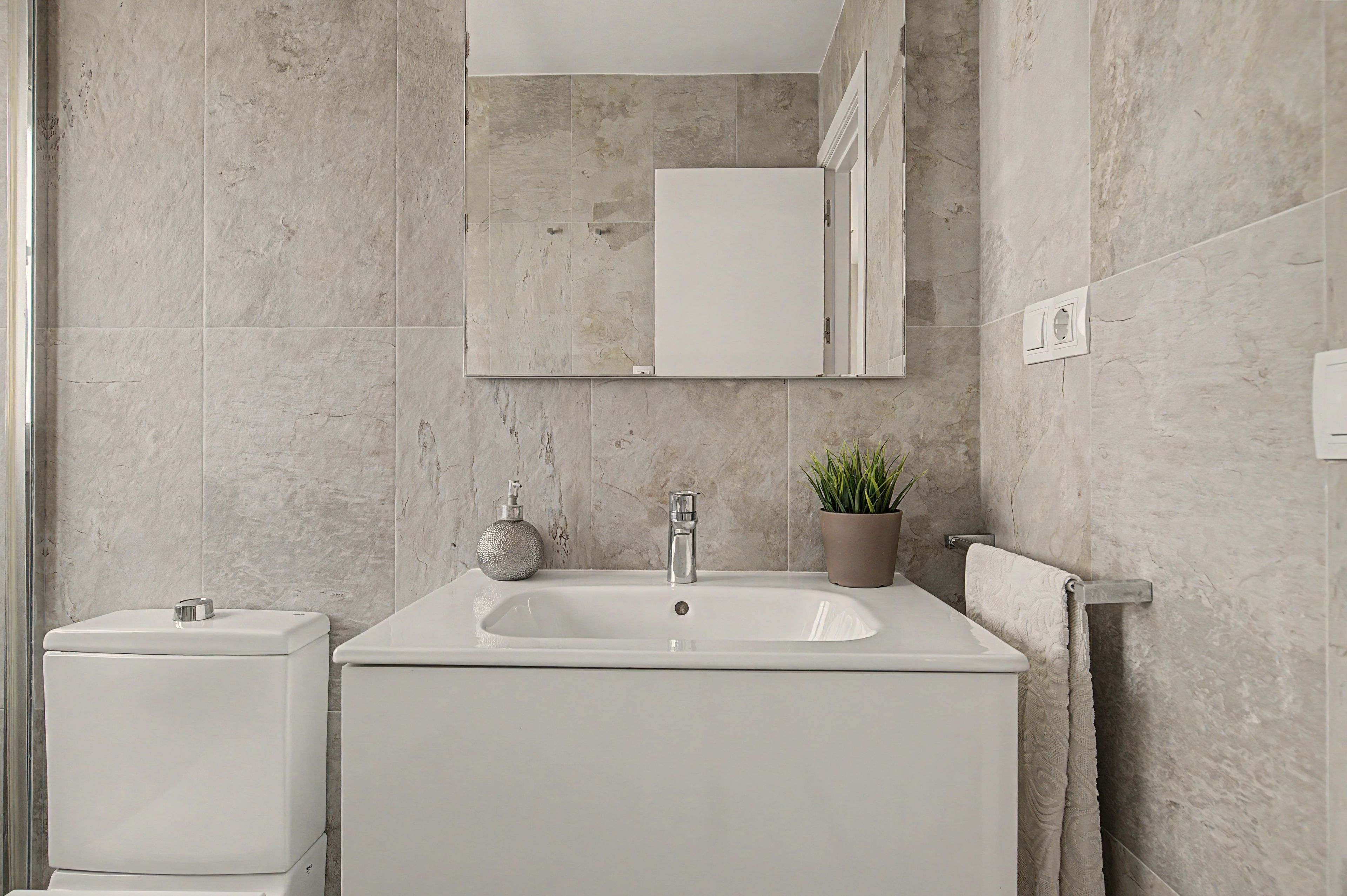 Un baño con lavamanos blanco, inodoro, espejo y planta en maceta.