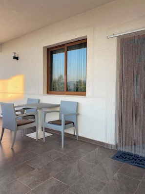 Uma sala de jantar com mesa e cadeiras, uma janela com cortinas, e uma porta com cortina decorativa.