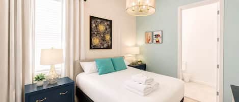 Un dormitorio con cama, mesitas de noche, un cuadro en la pared y una puerta.
