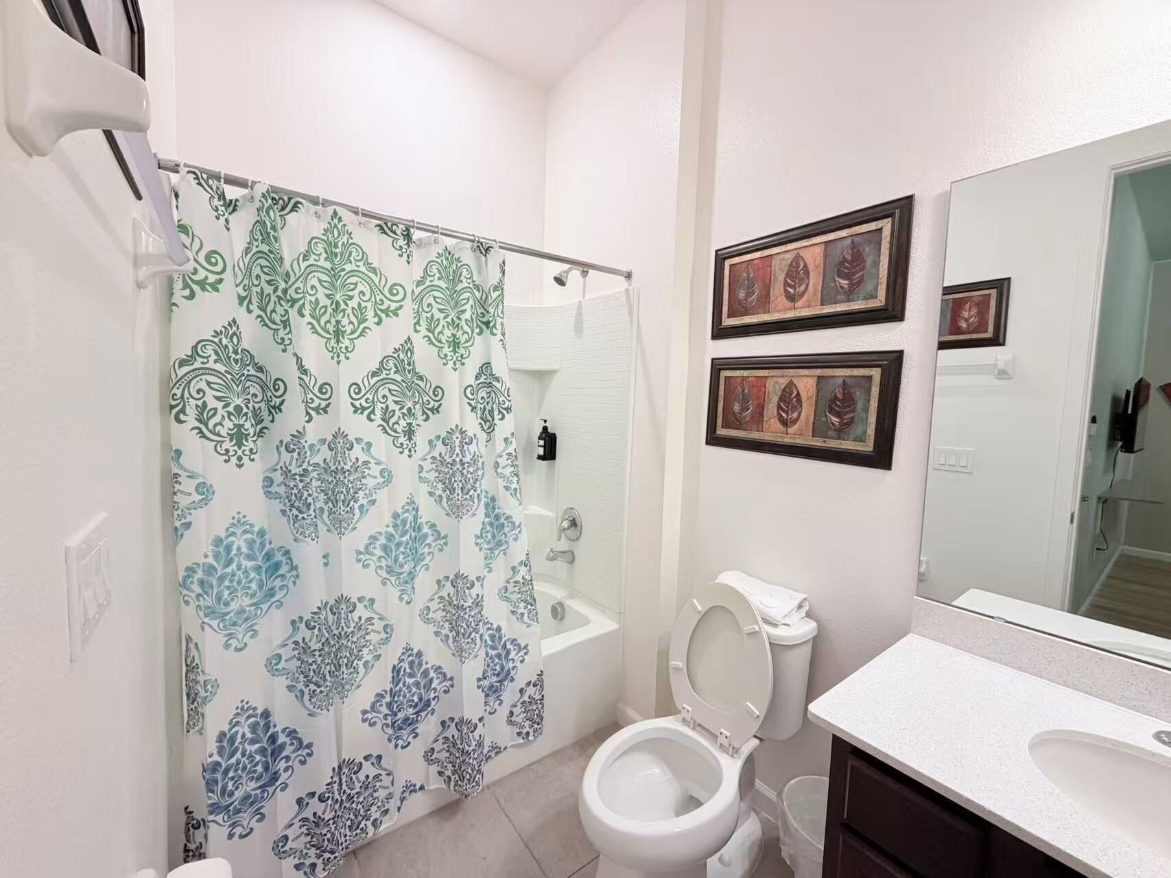 A bathroom with a shower curtain, toilet, sink, and framed artwork on the wall.